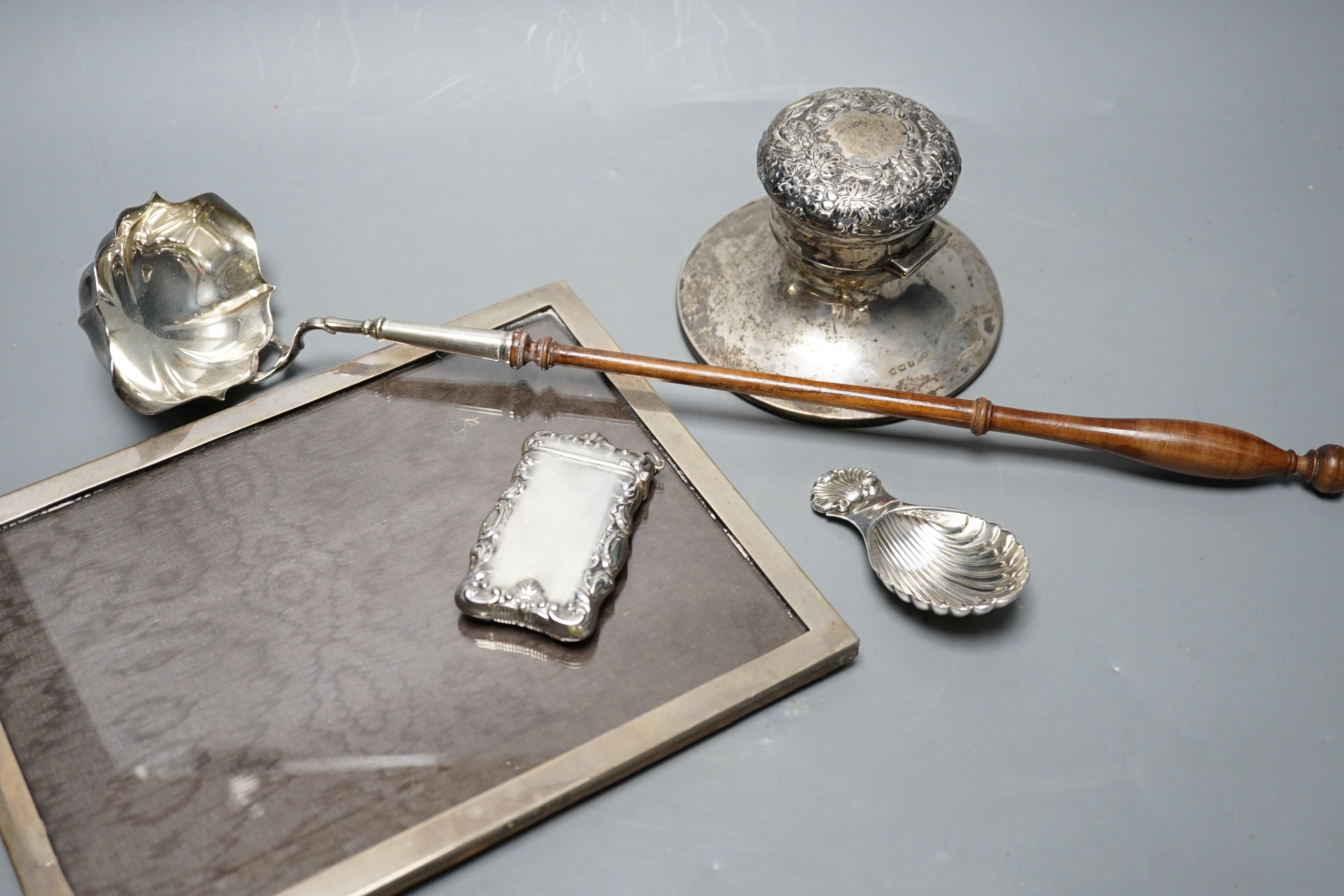 A silver mounted rectangular photograph frame, a modern silver mounted toddy ladle, a silver vesta case, a modern silver caddy spoon and a silver mounted inkwell.